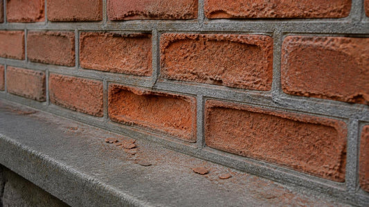 Old soft handmade brick wall where the brick faces have eroded and hollowed back while weathered gray cement repointing joints stand proud and intact above a stone ledge