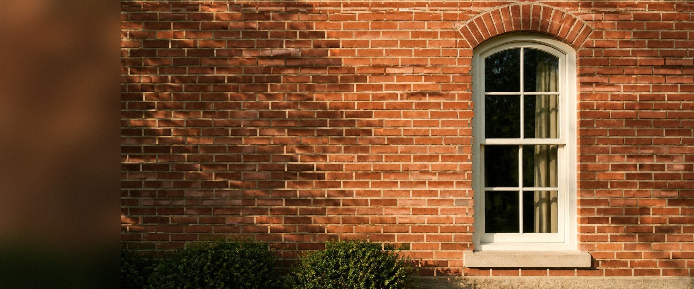 Red brick facade of a historic building with a tall arched white sash window
